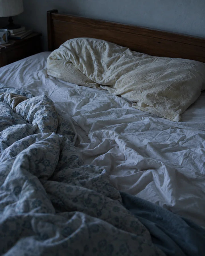 Cama desarrumada com um travesseiro velho, fino e amassado na cabeceira